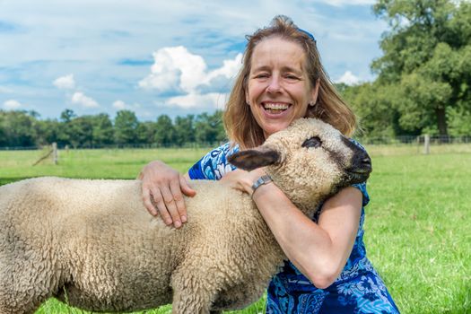 European woman embracing and hugging sheep in meadow