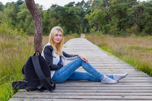 Blonde caucasian teenage girl resting on wooden footpath in forest area