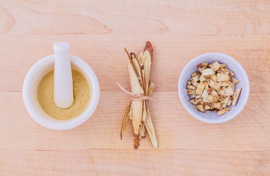 Licorice herbal medicine including powder, chopped and sliced root and mortar on wooden table