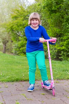 Young european girl standing with pink scooter in spring nature