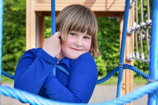 Young caucasian girl playing in web of blue ropes at playground