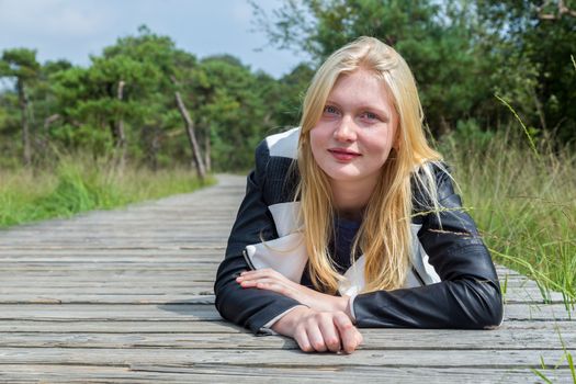 Blonde caucasian girl lying on wooden footpath in nature