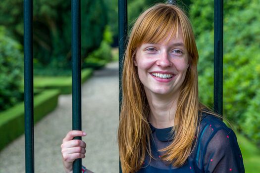 Red haired dutch teenage girl laughing holding metal bar of gate