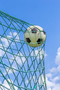 Black and white football caught in goal net with blue sky and white clouds