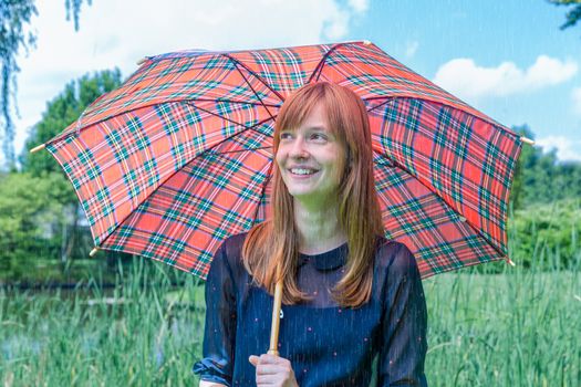 Caucasian teenage girl holding  umbrella on rainy day in green nature