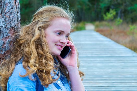 Blonde caucasian teenage girl phoning with mobile telephone in nature