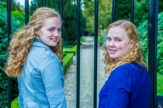 Two caucasian teenage sisterss looking back at fence of garden