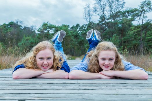 Two caucasian teenage girls lying on their belly on wooden footpath in nature