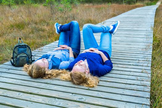 Two teenage girls lying on their backs on wooden path in nature