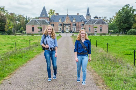 Two caucasian teenage girls walking away from castle in the netherlands