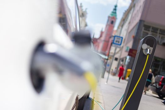 Power supply for electric car charging.  Urban electric car charging station on a city street. Close up of the power supply plugged into an electric car being charged.