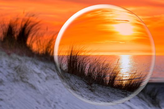 Crystal ball reflecting orange sunset at coast with sea dune and and beach