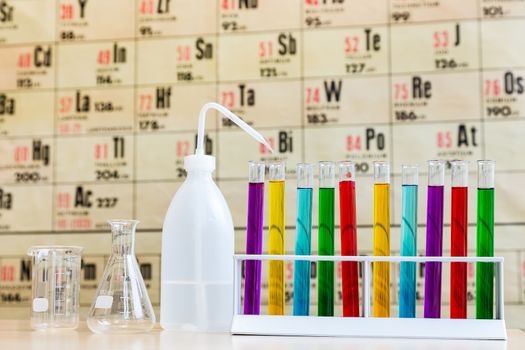 Chemistry with colored test tubes and glass in front of wallchart showing periodic table