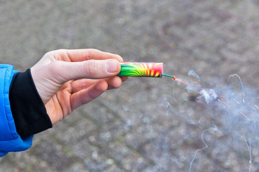 Hand of boy holding burning firework in street at  New Year's Eve