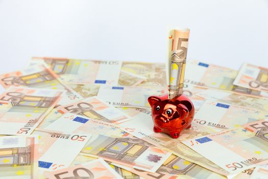 Small red piggy bank standing on many spread euro bills