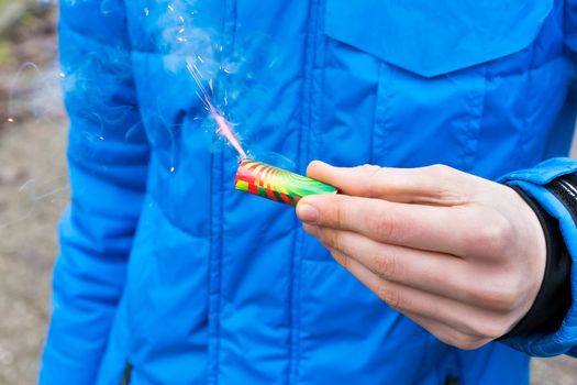 Hand of boy holding burning firework in front of blue jacket at New Year's Eve