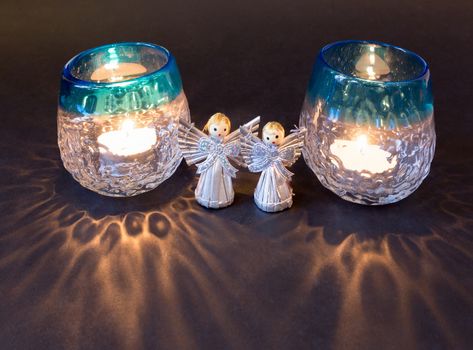 Two little angels and reflections of tea lights isolated on black background