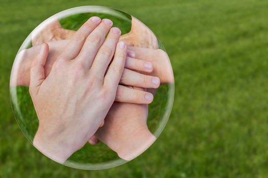 Hands uniting joining in glass ball isolated on green grass