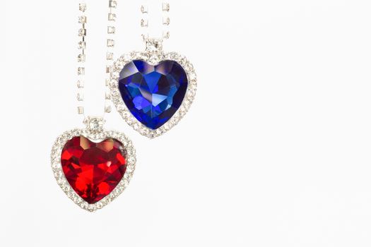 Two jewelry hearts blue and red hanging together as symbols isolated on white background