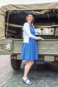 European middle aged woman dressed in blue clothes posing against military jeep
