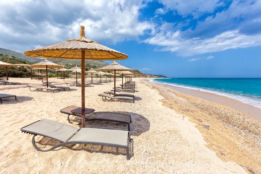 Beach umbrellas in rows for shade on sandy beach at coast with blue sea in Greece