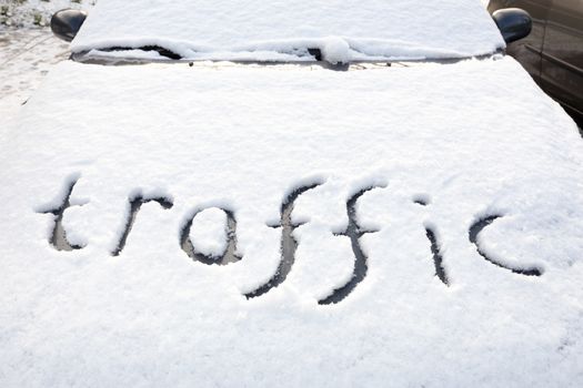 Word traffic written in snow on hood of car during winter season