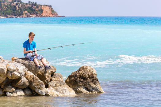 Caucasian teenage boy fishing with rod near sea and beach