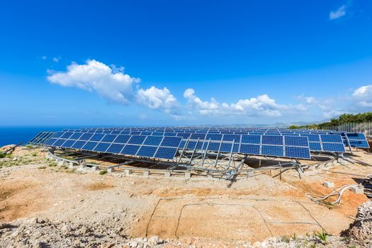 Field of many solar panels in rows on rotatable metal construction near blue sea in greece