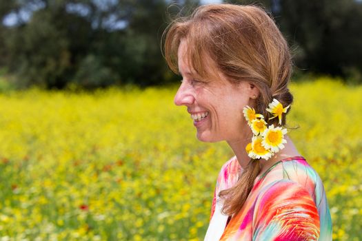 Caucasian middle aged woman wearing braid with yellow flowers near coleseed field in summer