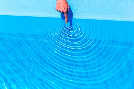 Forefinger making waves as circles in blue swimming pool