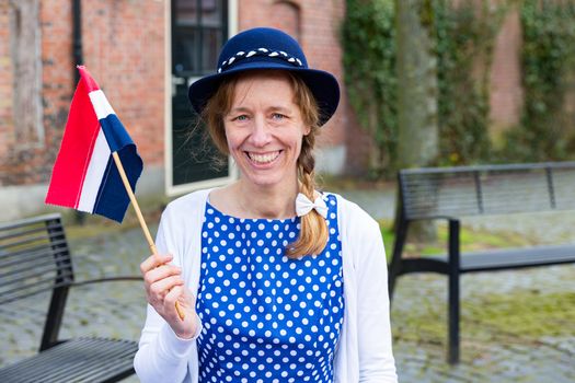 Caucasian middle aged woman dressed in blue clothes celebrating liberation day with dutch flag