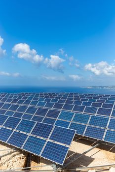 Field of many blue solar panels in rows near sea at coast in Greece with blue sky