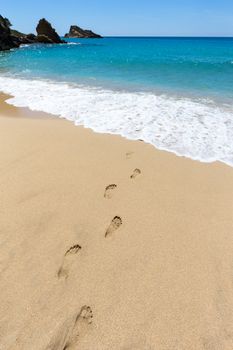 Footsteps in sandy beach leading to blue sea at coast on island in Greece