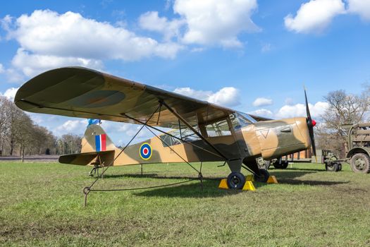 Old military airplane on green grass with blue sky and white clouds at exhibition outdoors