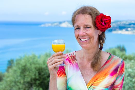 European middle aged woman with red rose holding drink near sea on vacation