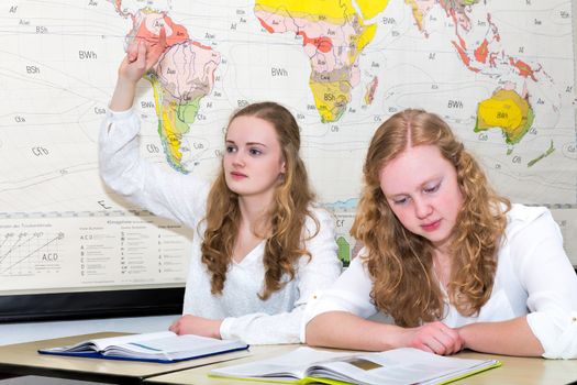 Caucasian teenage girl and student with learn finger in geography lesson in front of wall chart of the world