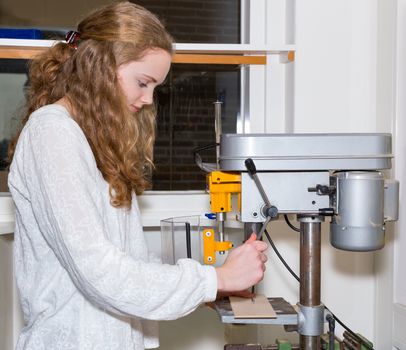 Caucasian teenage girl operating electric drilling machine in classroom at school