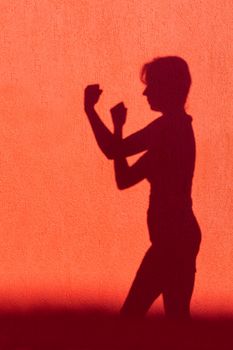 Silhouette of adult woman showing fists on red wall ready to fight