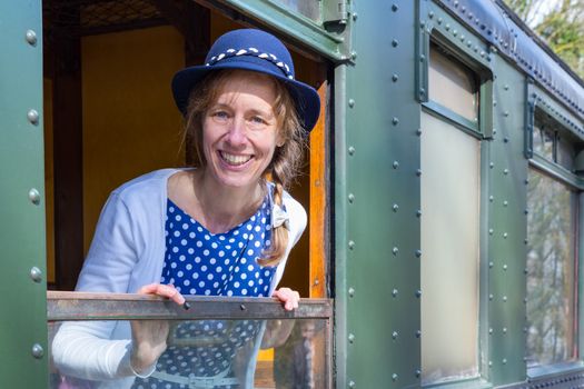 Caucasian middle aged woman dressed in blue old-fashioned clothes in window of steam train
