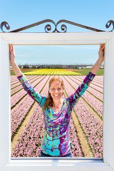 Happy caucasian middle aged woman standing in window at pink flowers field in Holland