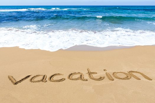 Word vacation written in sandy beach at coast with blue sea and waves