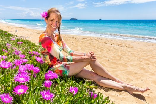 Woman with pink flowers on sandy beach with blue sea