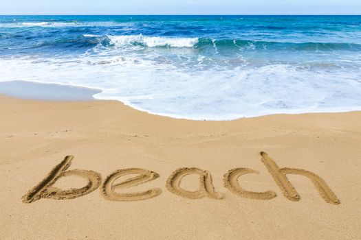 Word beach written in sandy coast with blue sea