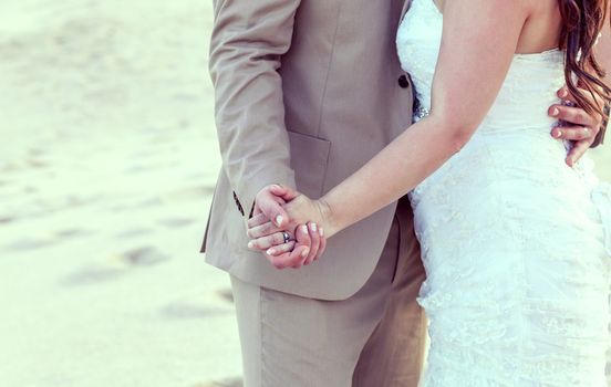 
Bride and groom's hands with wedding rings on tropical beach.