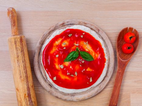 Pizza dough with tomato sauce preparation on wooden table