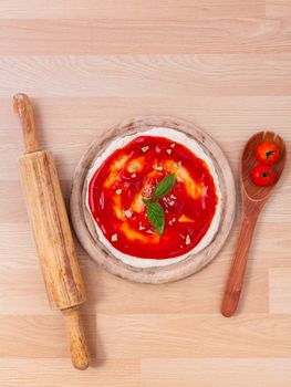 Pizza dough with tomato sauce preparation on wooden table