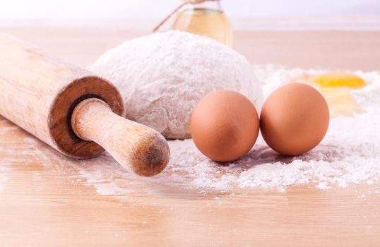 Baking ingredients including fresh eggs, flour and a rolling pin on wooden table.