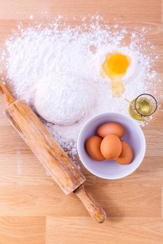 Baking ingredients including fresh eggs, flour and a rolling pin on wooden table.