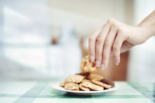 Human hand taking cookie in plate on a table