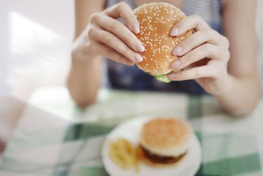 Woman holding hamburger and sitting at the table